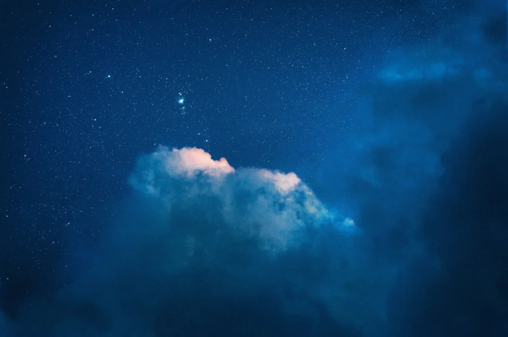 A phot of fluffy white clouds on a starry night during blue hour